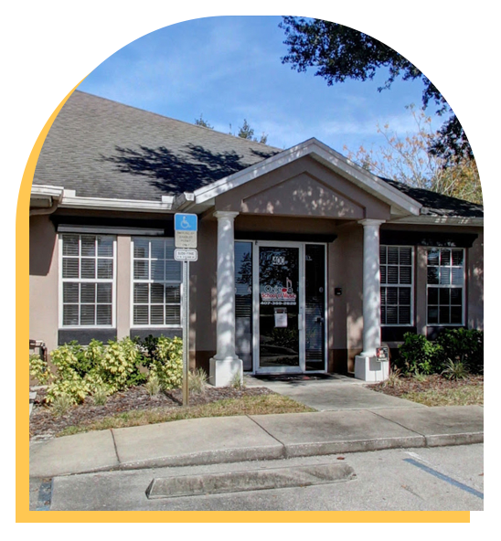 A single-story music school with columns at the entrance, large front windows, a glass door, and a handicapped parking sign by the curb. Shrubs and trees line the building under a clear blue sky—perfect for Step Up music lessons.